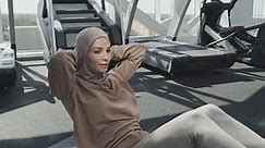 Young Muslim woman in hijab doing v-sits exercise on mat while having ab workout in gym