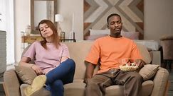 Un jeune couple, un homme noir et une femme blanche sont assis l'un à côté de l'autre sur le canapé et attendent quelque chose