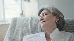 An elderly woman is snoozing in a comfortable chair, relaxing and resting her energy, thinking about pleasant things and doing breathing exercises for harmony and balance. Healthy grandmother.