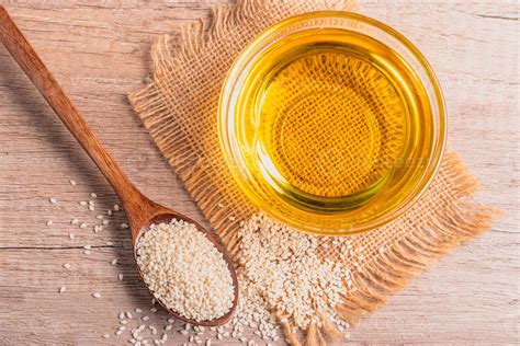 sesame oil in a bowl and white sesame seeds on wooden background ...