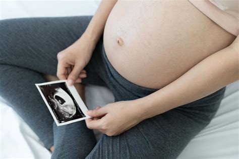 A pregnant woman is looking at an ultrasound photo of fetus. Mother ...