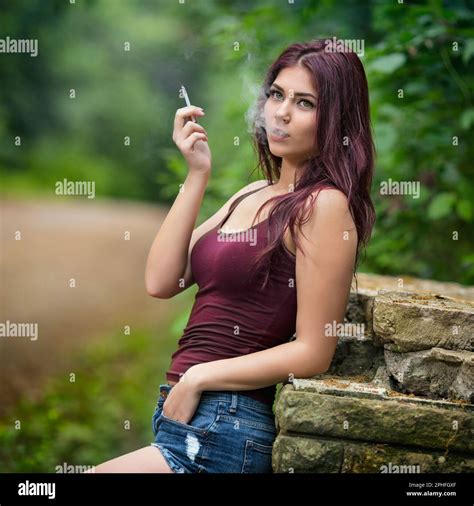 An attractive young woman with red hair smoking a cigarette while enjoying a leisurely stroll in ...