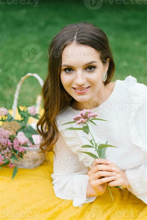 A beautiful young woman with natural nude makeup holds a spirea flower in her hands, lying on a ...