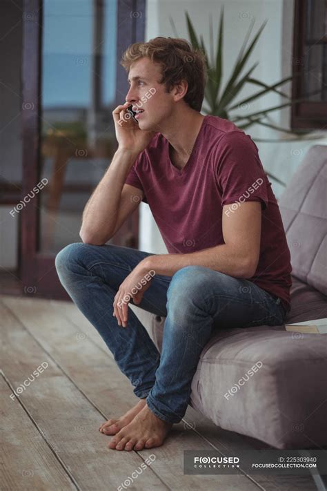 Man sitting on sofa and talking on mobile phone in living room — Abode ...