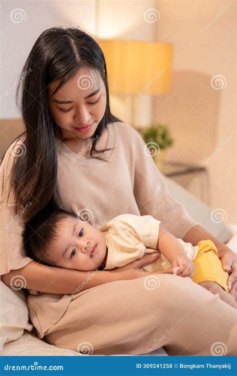 A Caring Asian Mom is Putting Her Little Son To Sleep in Her Arms ...
