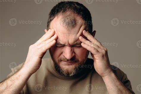 A man has a severe headache. He holds his head in his hands and ...