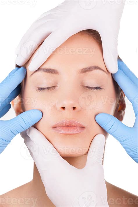 Handmade beauty. Beautiful young woman keeping eyes closed while four hands in medical gloves ...