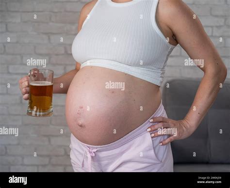 Faceless pregnant woman with rash on stomach holding glass of beer ...