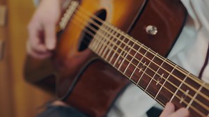male hand rearranges chords on acoustic guitar close up.