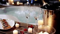 Champagne glass, food and hot tub couple arrive, enter and romantic partner bonding on Valentines day date. France holiday night, candle flame and marriage people enter jacuzzi with alcohol and snack
