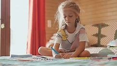 Cute girl drawing sitting lotus position. Adorable preschool girl in casual clothes sitting on bed and drawing in book with felt-tip pens while studying at home