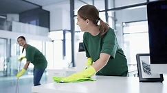 Office building, cleaner or happy woman cleaning as a team to wipe a dusty, dirty or messy table together. Cleaners, service or employees with smile working or washing bacteria off desk or furniture