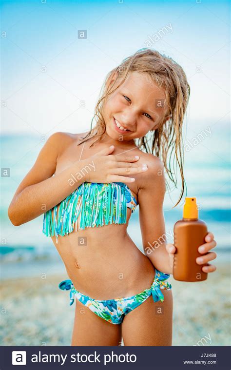 Peeping through the hole in the wall in the beach cabin. Cute little girl applying suntan lotion on the beach and ...