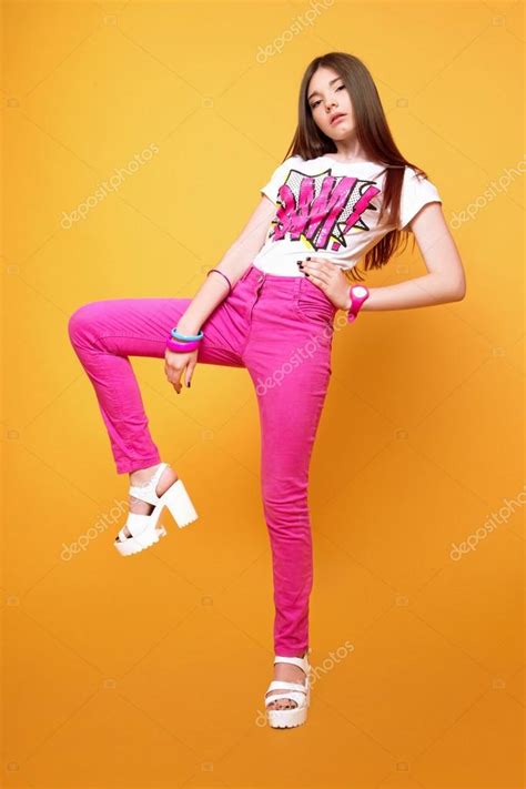 This website requires you to be 21 years of age or older. A beautiful 13-years old girl dressed in pink pants and a T-shirt in studio on yellow background ...