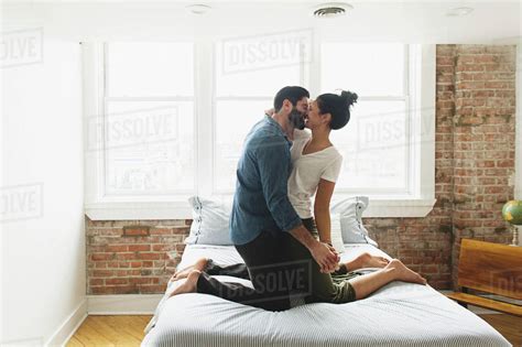 Romantic couple kissing while kneeling on bed at home - Stock Photo - Dissolve