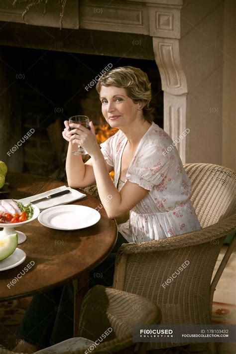 Portrait of smiling mature woman sitting at laid table holding glass of ...