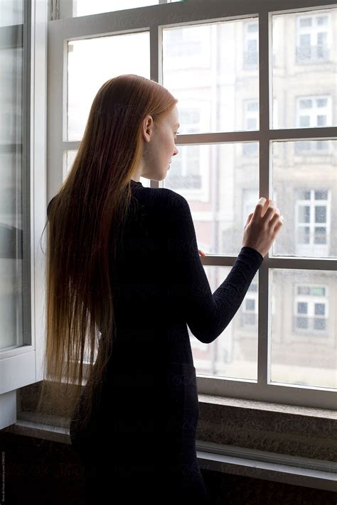 young-woman-standing-at-window,-looking-out-by-rene-de-haan-redhead