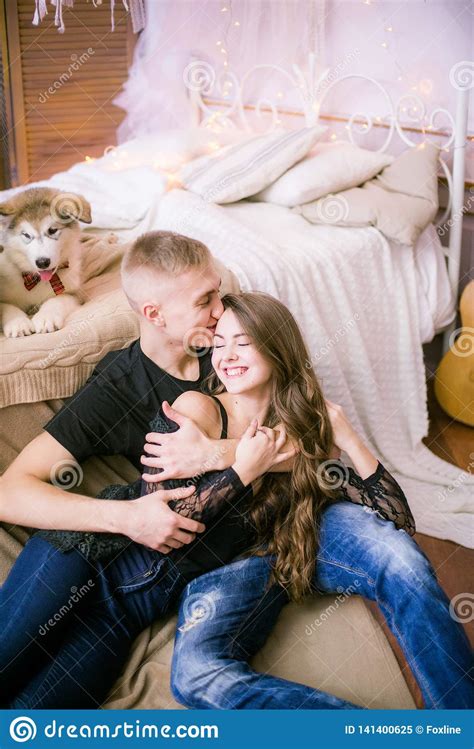 Joyful Young Loving Couple Sitting In The Bedroom While Expressing Love With Puppies Stock Image ...