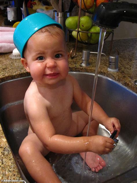 Sudsy crying baby in sink full of water not quite ready to continue his bath. Baby Katie Rockwell