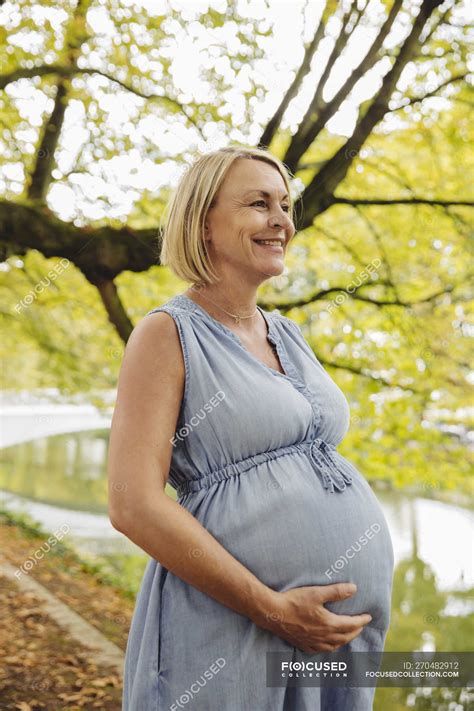 Happy mature pregnant woman standing in park — Three Quarter Length ...